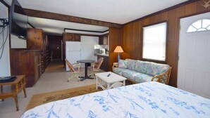 A compact room with a bed, a sofa, a small table, and a chair. There is a kitchenette area with a refrigerator, a microwave, and a sink. A television is mounted on the wall. - Bayshore Drive 211 3 Bedroom Home by RedAwning (Ocean City)