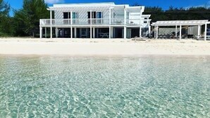 A beachfront property with a large house, clear water, and a sandy beach. - Caribbean Sandcastle 4 Bedroom Home (Governor's Harbour)