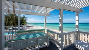 A covered outdoor area with a pool, wooden deck, and a view of the ocean. - Caribbean Sandcastle 4 Bedroom Home (Governor's Harbour)