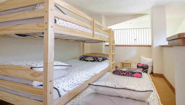 A bunk bed room with star-patterned bedding, a small table with a clock, and a window with a view of the sky.