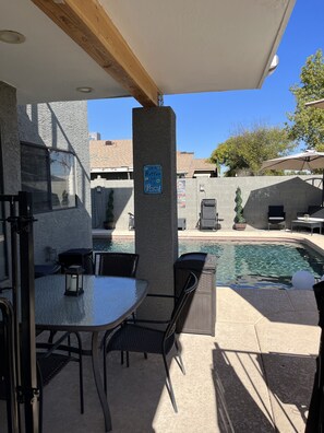 An outdoor patio area with a pool, a table with chairs, and a sign that reads "Life is Better by the Pool."
