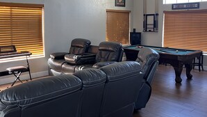 A spacious living room with a pool table, leather seating, and a ceiling fan. - Remodeled 2 story home w/ pool 8 minutes from the State Farm Stadium! (Glendale)