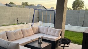 A covered outdoor seating area with a sectional sofa, two round tables, and a fire pit. - Remodeled 2 story home w/ pool 8 minutes from the State Farm Stadium! (Glendale)