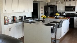 A modern kitchen with white cabinets, a central island with bar stools, stainless steel appliances, and pendant lighting. - Remodeled 2 story home w/ pool 8 minutes from the State Farm Stadium! (Glendale)