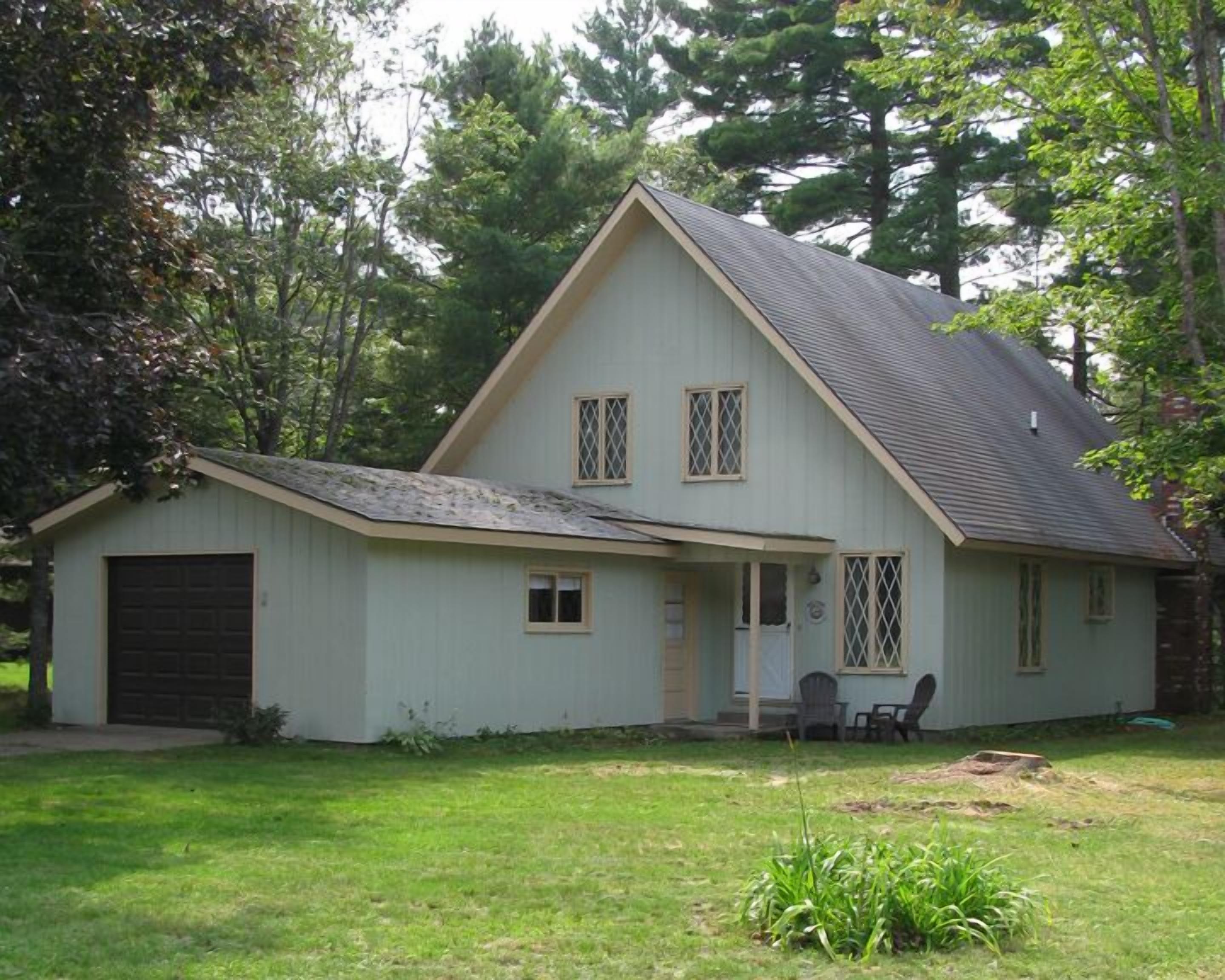 A two-story house with a sloped roof, a front garage, and a small porch with chairs.