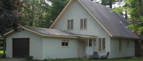 A two-story house with a sloped roof, a front garage, and a small porch with chairs.
