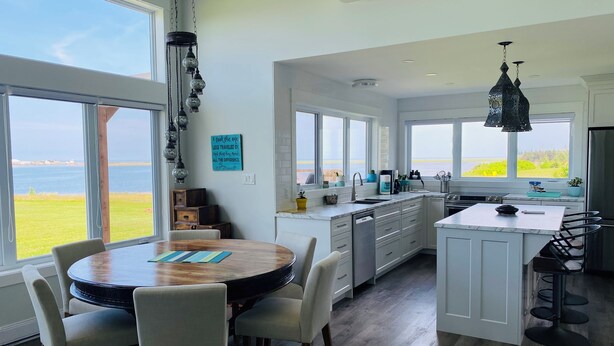 Eine moderne Küche mit großen Fenstern, einem Essbereich und Blick auf das Meer.