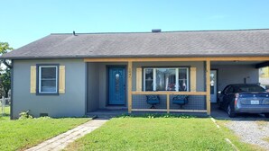 Een gelijkvloers huis met een overdekte veranda, een blauwe deur en een auto op de oprit.