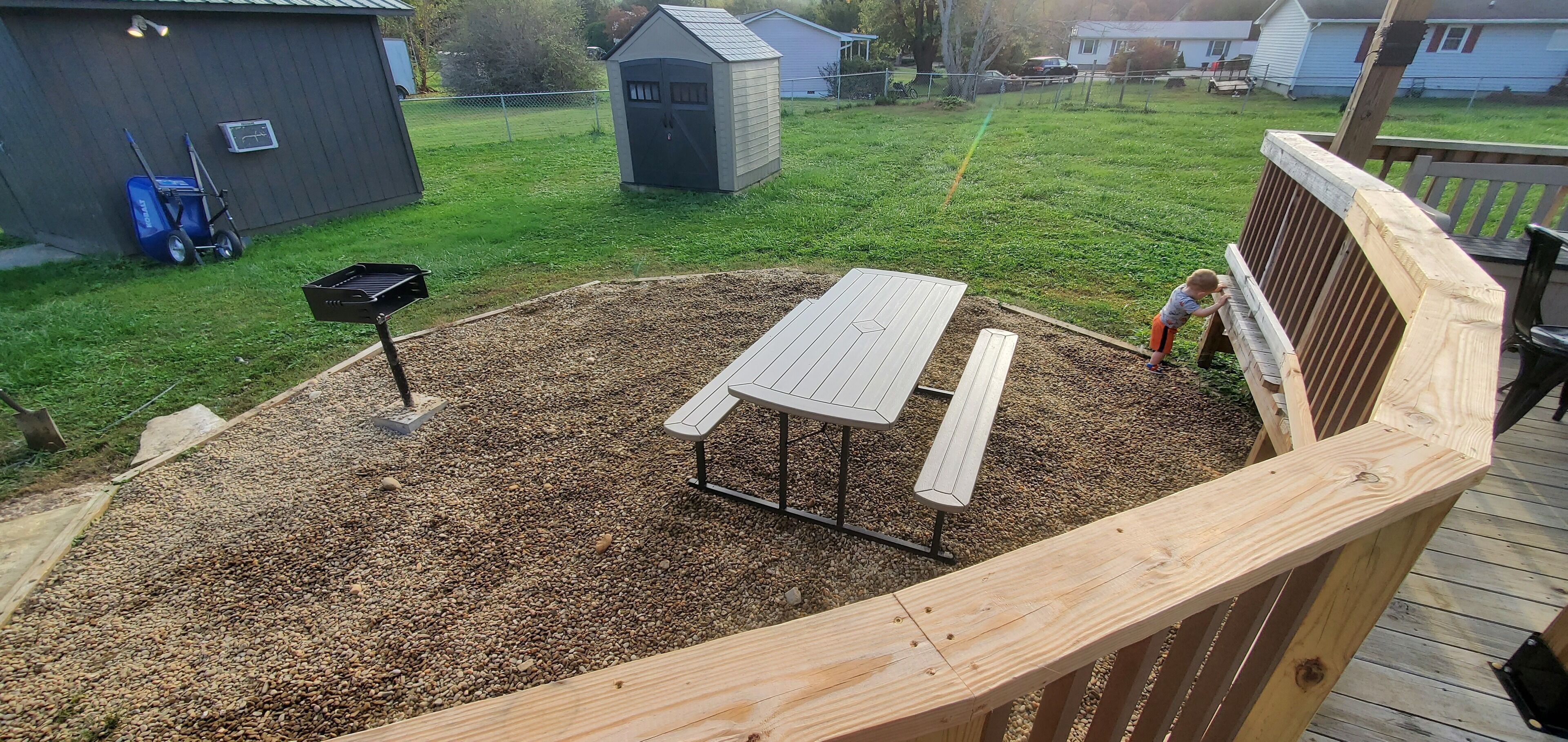 A wooden deck with a picnic table and benches, surrounded by a gravel area.