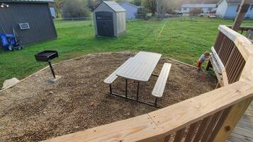 A wooden deck with a picnic table and benches, surrounded by a gravel area.