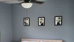 Een slaapkamer met een bed, een plafondventilator, bedlampjes en ingelijste foto’s aan de muur.