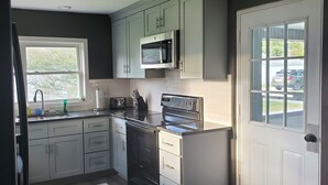 Een moderne keuken met witte kasten, een inbouwmagnetron, een fornuis en een raam.