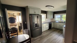 Een moderne keuken met een ingebouwde wasmachine en droger, roestvrijstalen apparatuur en een groot raam dat natuurlijk licht binnenlaat.