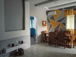 Un'area pranzo con un tavolo rotondo e sedie in vimini, un condizionatore d'aria a parete e una parete con motivo geometrico.