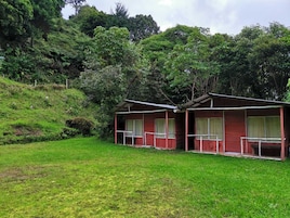 Uma cabana pequena com telhado vermelho, varanda e área gramada na frente.