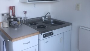 Cocina compacta con microondas, pileta y hornilla. Hay alacenas sobre la hornilla y un reloj en la pared.