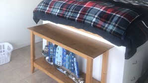 Un dormitorio con cama, un banco de madera, una estantería con objetos decorativos y una puerta.