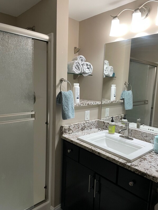 A bathroom with a white sink, dark cabinets, a glass shower door, and a mirror with lights. - Mid Mod,Great Location, Heart of downtown Knoxville (Knoxville)