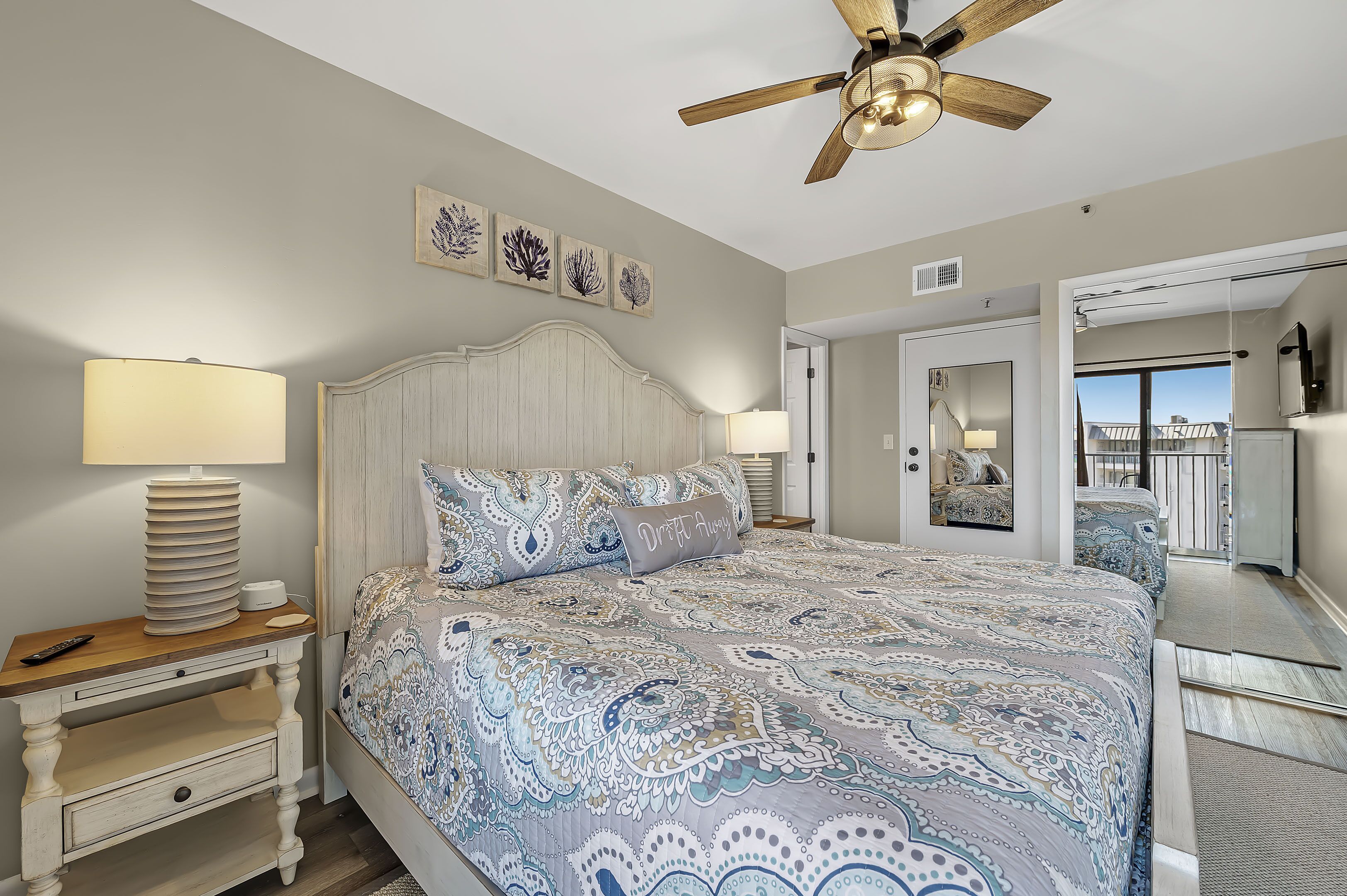 A bedroom with a large bed, a ceiling fan, and artwork on the wall.