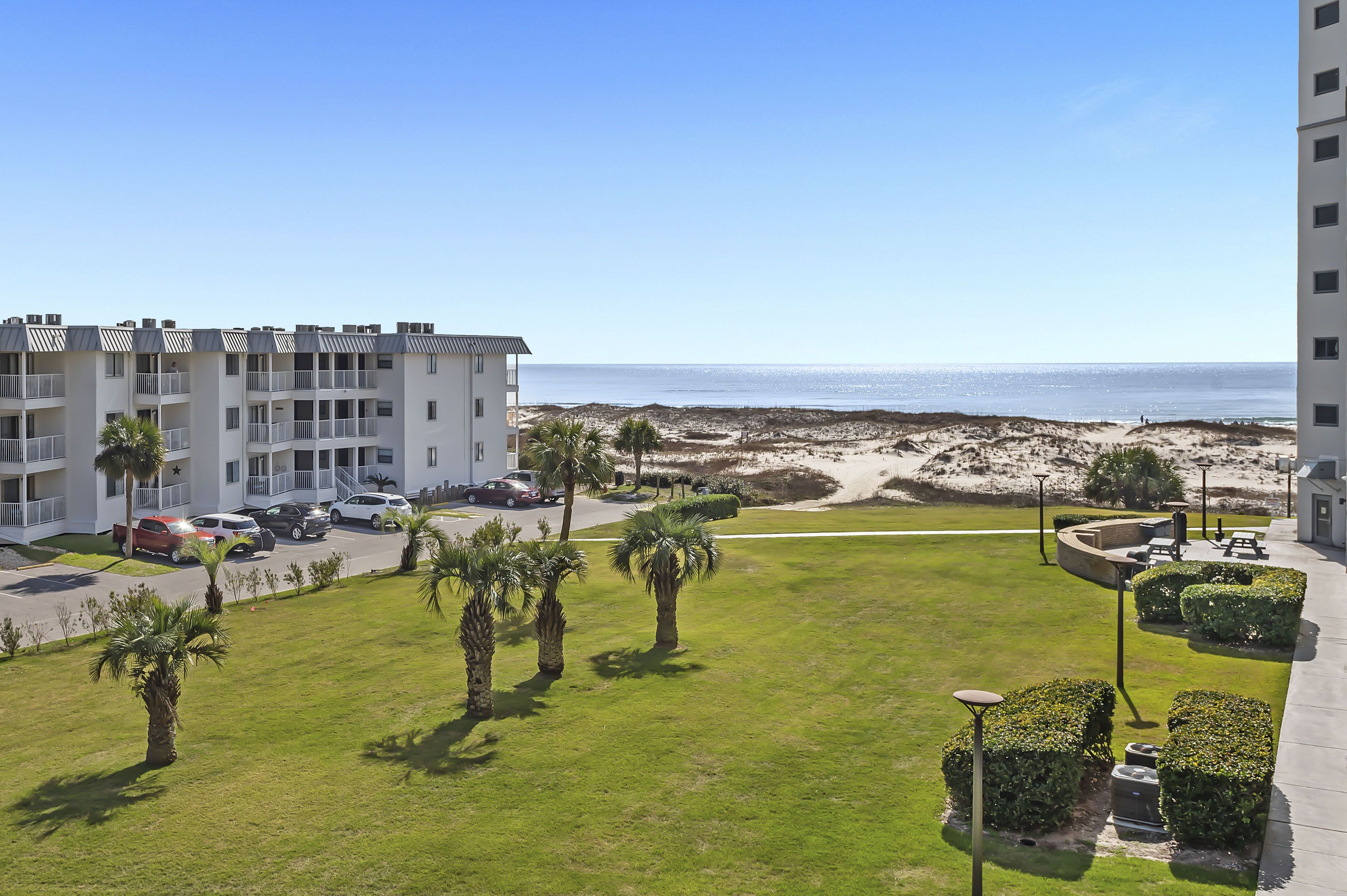 A multi-story building with a parking area, palm trees, and a view of the beach.