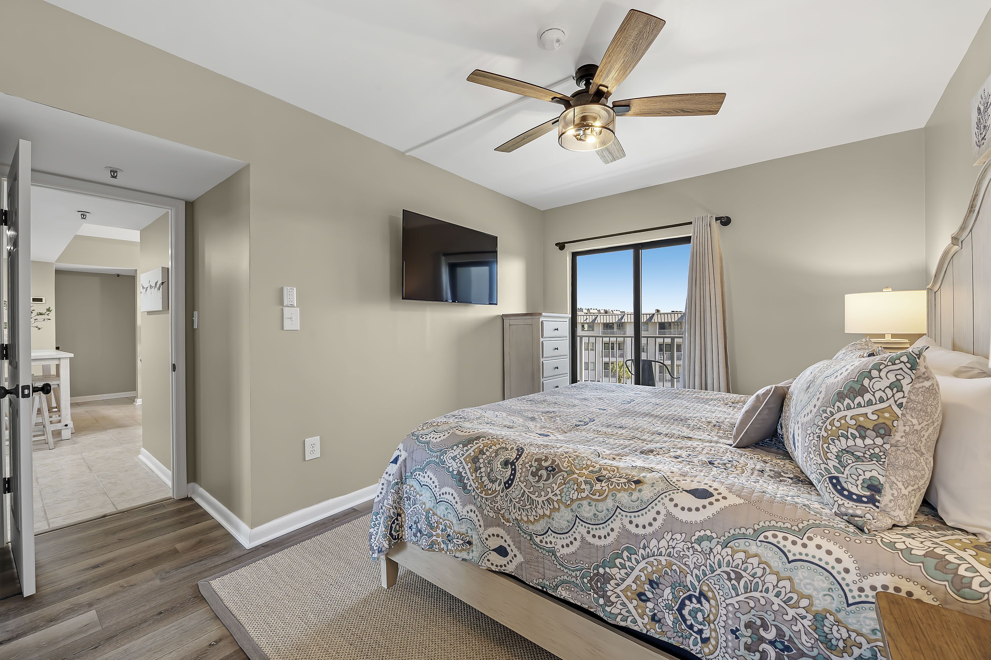 A bedroom with a bed, a ceiling fan, a TV, and a window with curtains.