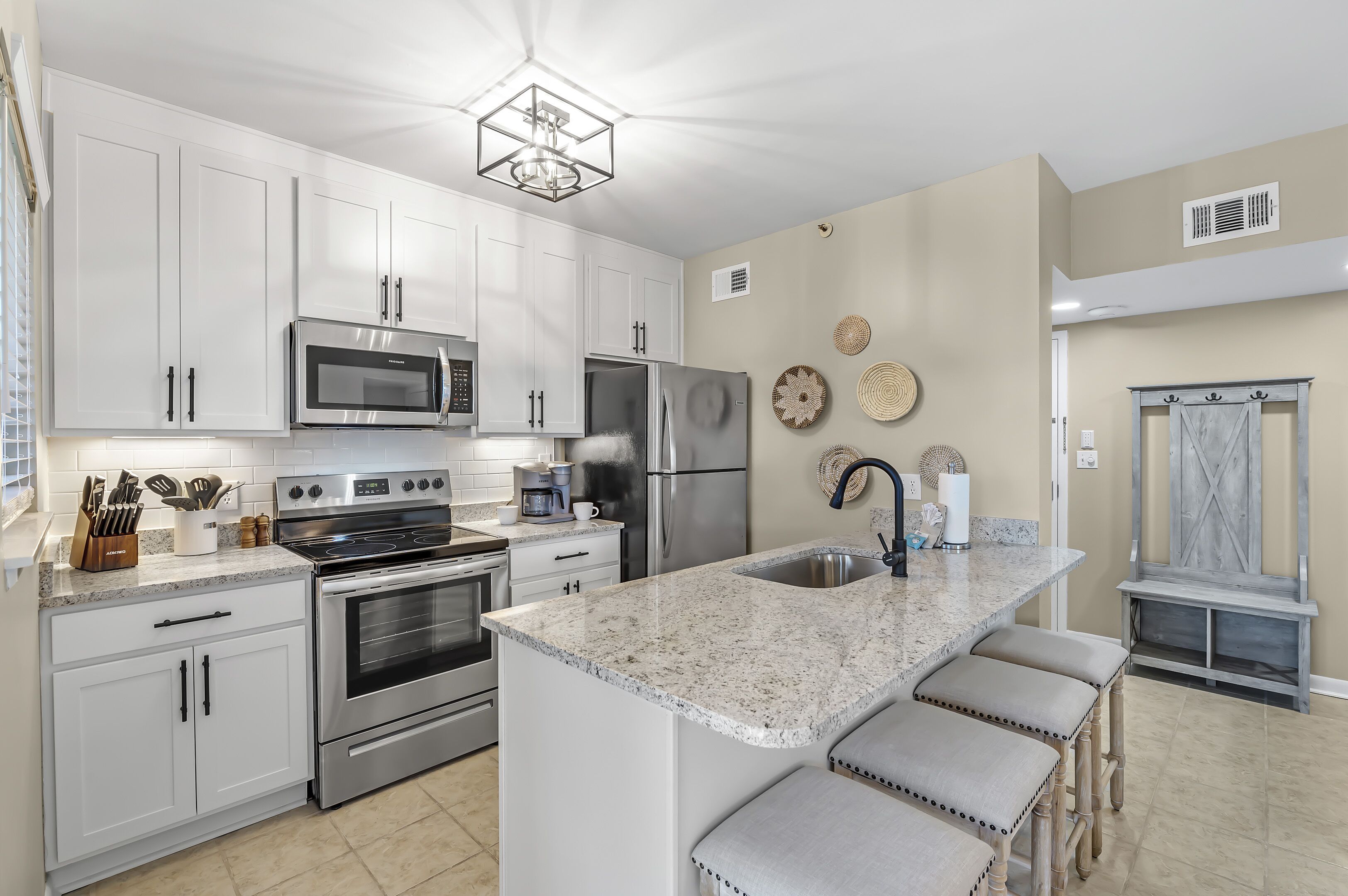 A modern kitchen with white cabinets, stainless steel appliances, a granite countertop, and a bar area with stools.