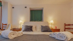 Ein Hotelzimmer mit einem Bett, zwei Nachttischlampen, einem grünen Vorhang und aufgerollten Handtüchern auf dem Bett.