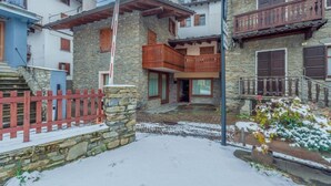 Ein Steinhaus mit einem hölzernen Balkon, einem roten Zaun und Schnee auf dem Boden.