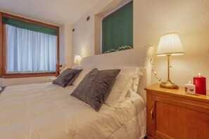 A hotel room with a bed, a nightstand with a lamp, a window with curtains, and a green wall.