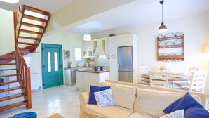 Un vaste espace de vie comprenant un canapé, un escalier en bois, une cuisine avec des meubles blancs et un coin repas avec une table et des chaises.