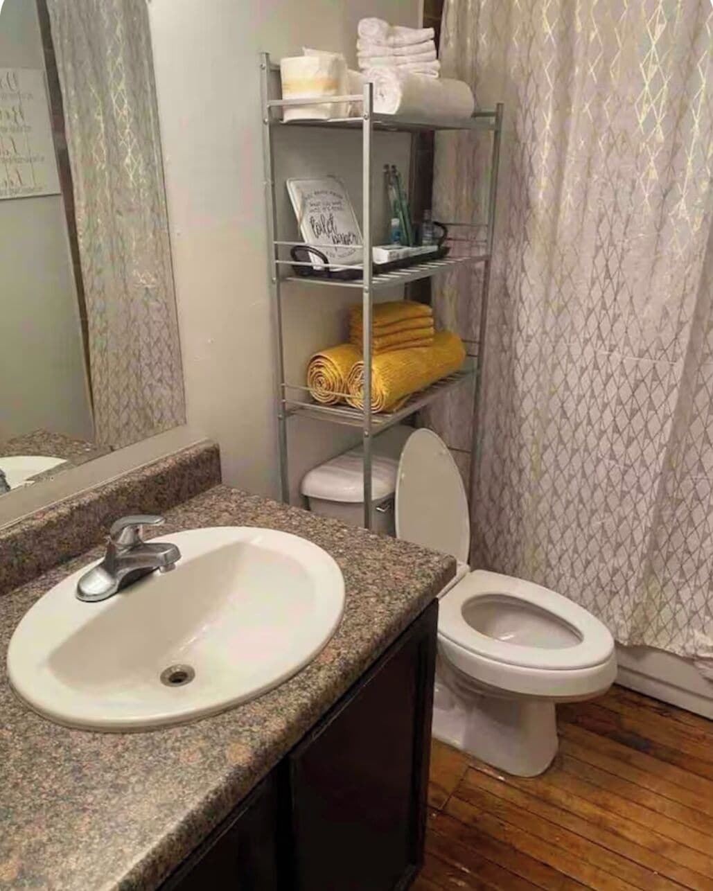 A bathroom with a granite countertop sink, a white toilet, and a metal shelf with towels and toiletries.
