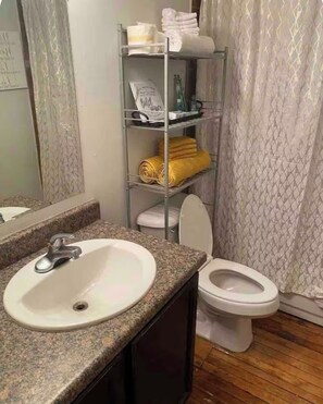 A bathroom with a granite countertop sink, a white toilet, and a metal shelf with towels and toiletries.
