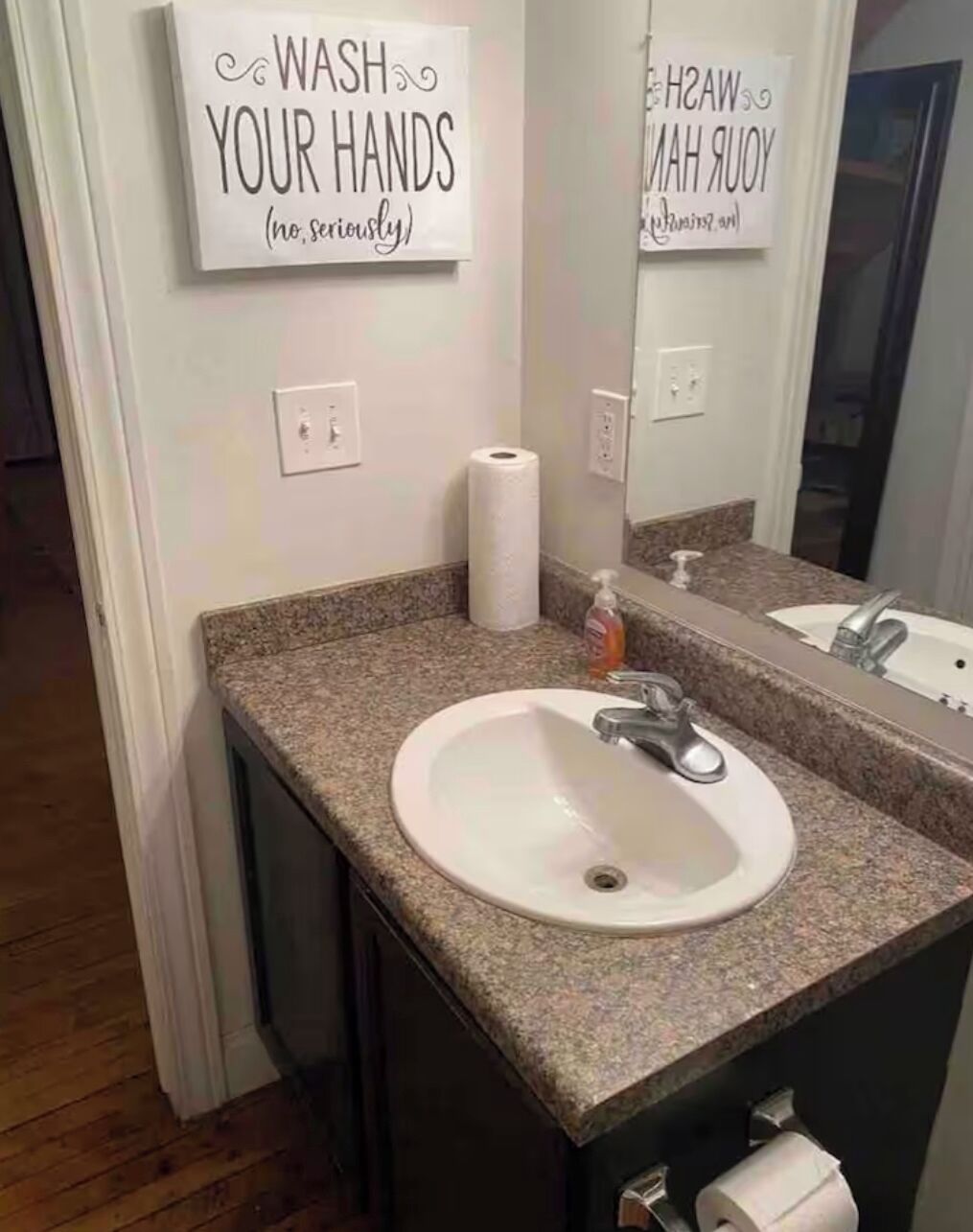 A bathroom with a granite countertop, a white sink, a mirror, and two signs on the wall.