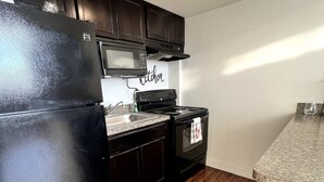 A compact kitchen with dark cabinets, a black refrigerator, a microwave, and a stove. - Open Loft w/Water Bridge View 2mins to Dwntn (Detroit)