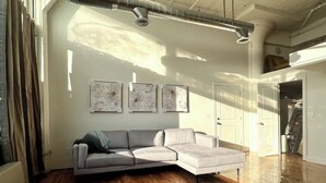 A modern living room with a sectional sofa, wooden flooring, and three abstract wall art pieces. - Open Loft w/Water Bridge View 2mins to Dwntn (Detroit)