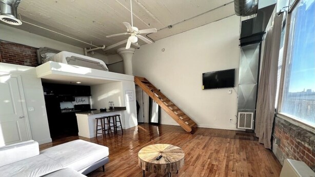A modern loft apartment with a loft bed, a kitchen area, a dining space, and a large window offering a city view. - Open Loft w/Water Bridge View 2mins to Dwntn (Detroit)
