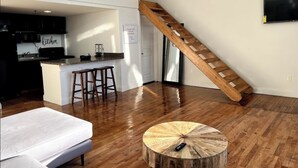A loft-style apartment with a kitchen, a wooden staircase, and a round wooden coffee table. - Open Loft w/Water Bridge View 2mins to Dwntn (Detroit)