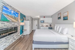 Habitación de hotel con pared de piedra, una cama, un televisor, un microondas, un refrigerador y una pequeña cocina.