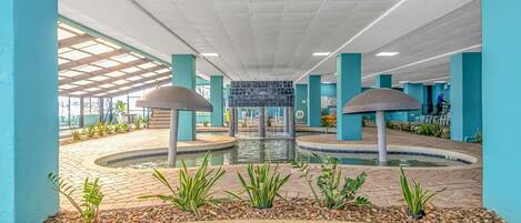 Un área de piscina con una fuente central, rodeada por un solárium alicatado y sostenida por columnas.