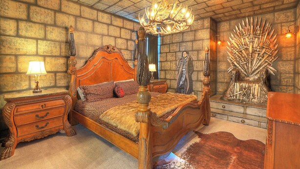 Un dormitorio con cama con dosel, candelabro, un gran tapiz y una silla similar a un trono.