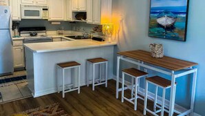 Une cuisine moderne avec des meubles blancs, un îlot central doté de tabourets, un four à micro-ondes et un évier.
