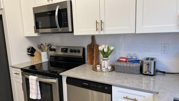 Una cocina moderna con electrodomésticos de acero inoxidable, armarios blancos y encimera de mármol.