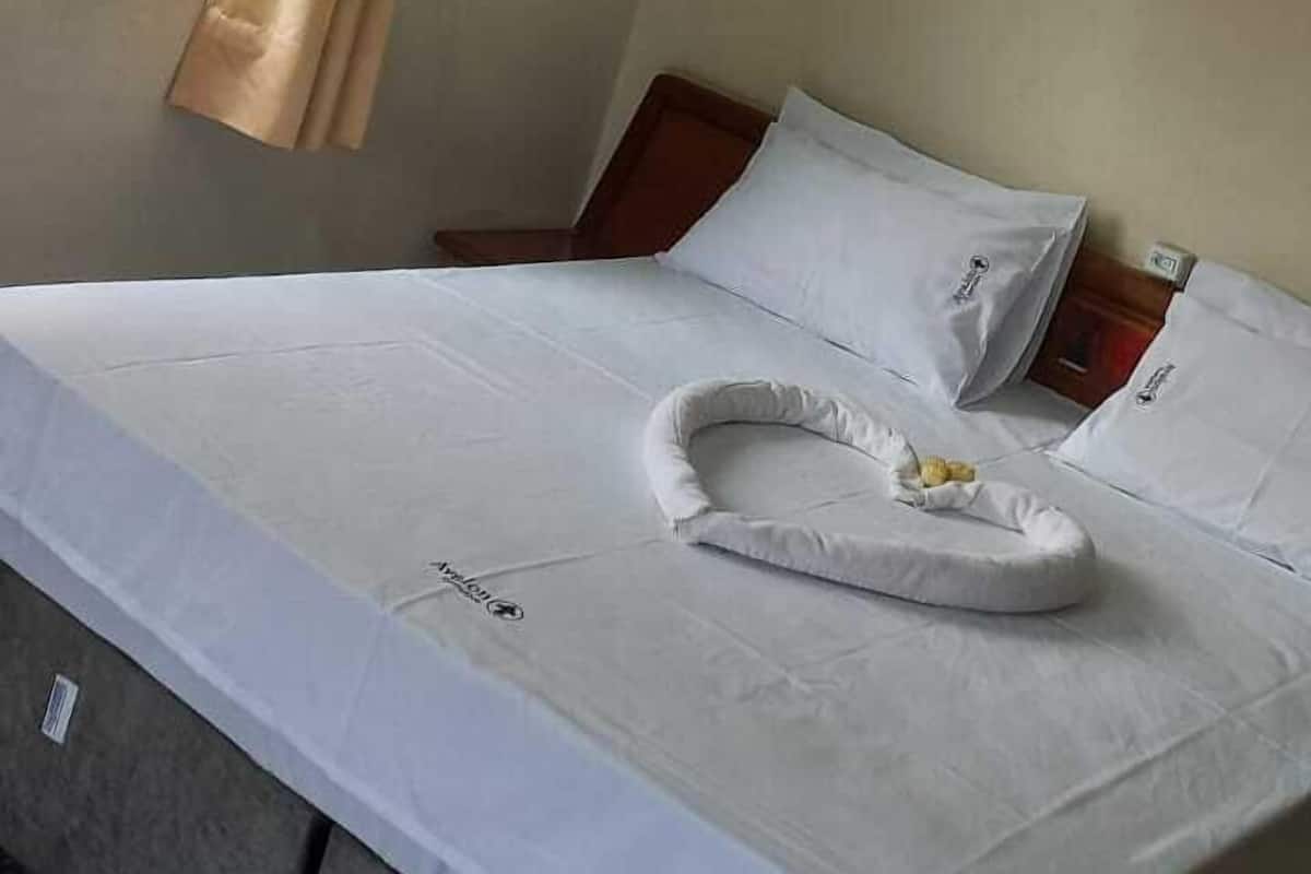 A hotel room with a bed, a window with curtains, a ceiling light, and a wall-mounted light fixture.