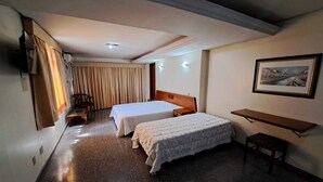A hotel room with two beds, a desk, a chair, a TV, and a painting on the wall. - Avalon (Goiânia)