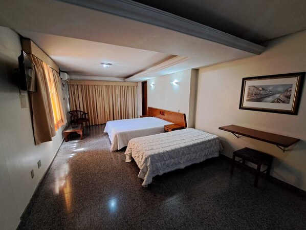 Habitación de hotel con dos camas, un escritorio, una silla, un televisor y un cuadro en la pared.