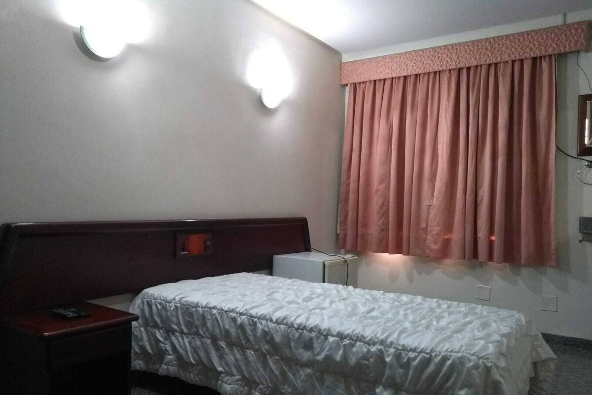 A hotel room with a bed, bedside table, and a window with curtains.