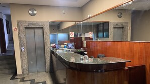 A reception area with a marble counter, wooden paneling, and two elevators. - Avalon (Goiânia)
