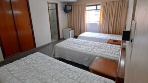 A hotel room with two single beds, a television, a wardrobe, and a window with curtains. - Avalon (Goiânia)