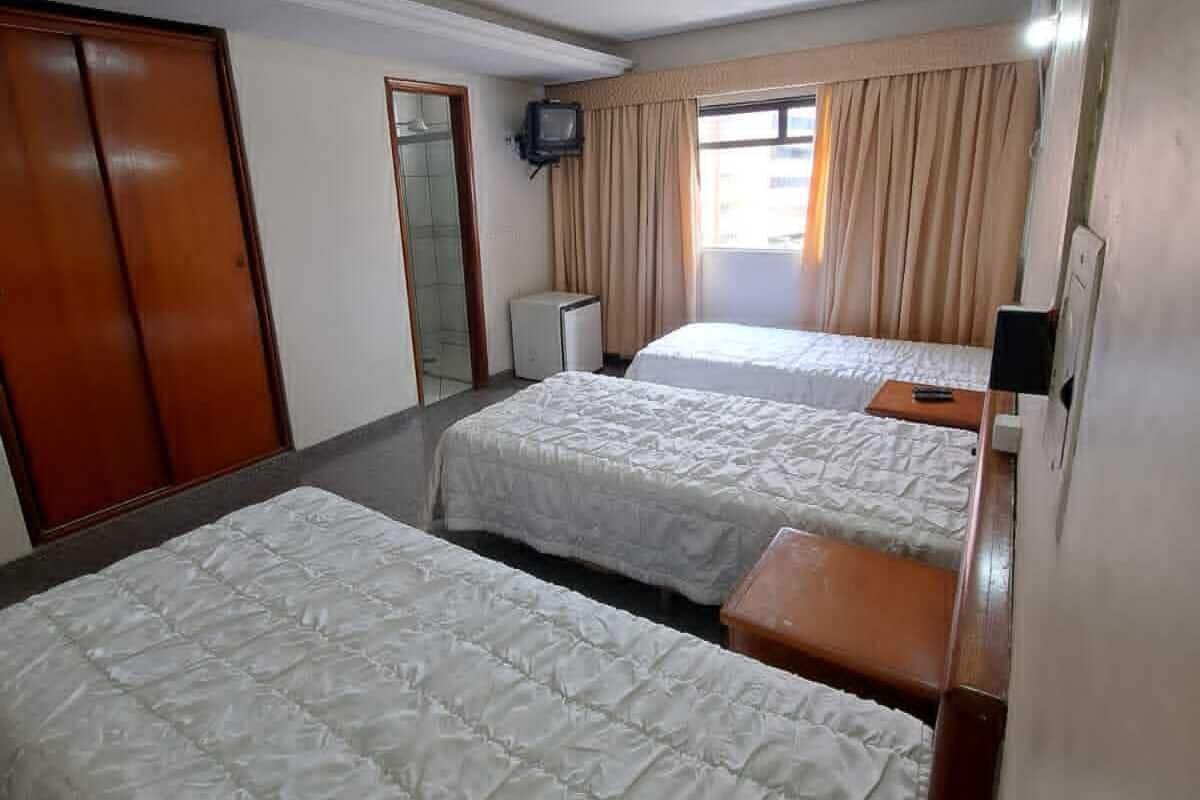 A hotel room with two single beds, a television, a wardrobe, and a window with curtains.