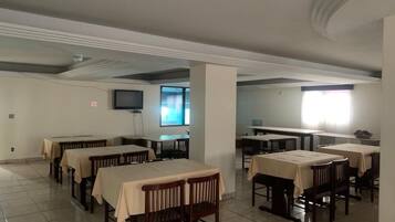 Zona pranzo con diversi tavoli e sedie, una televisione montata a parete e una finestra che offre luce naturale.